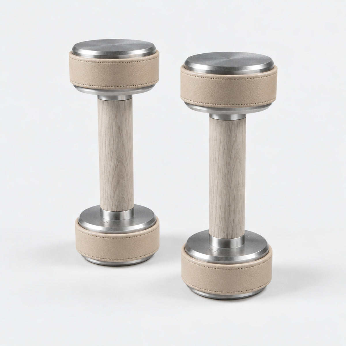 Nak Dumbbell Pair — angled view; Grey Ash wood, beige leather and natural stainless steel where applicable. FYSIK studio finish study — October 2026. Representative configuration.